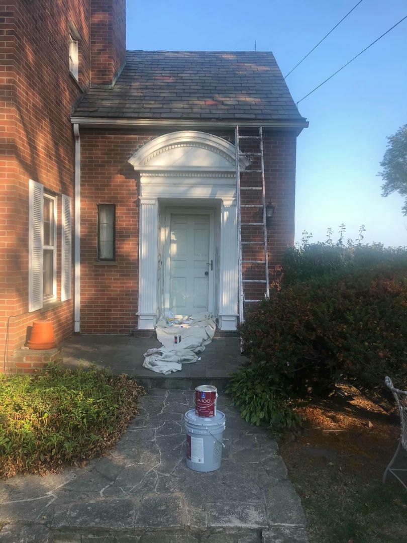 A bucket of paint is sitting on the sidewalk in front of a brick building.