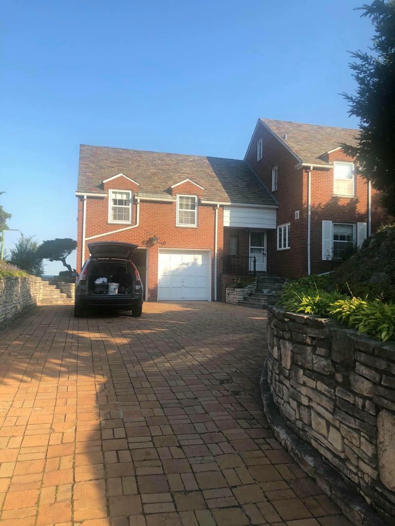 A car is parked in front of a large brick house.