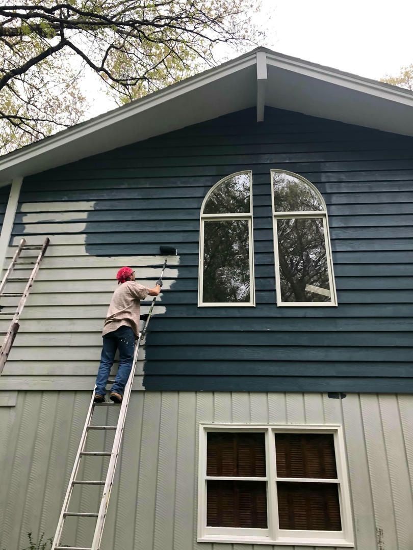 A woman is painting the side of a house with a ladder.