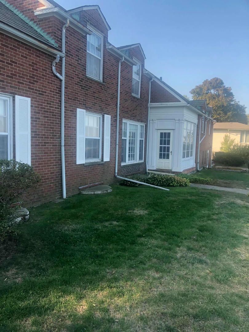 A large brick building with white shutters and a large lawn in front of it.