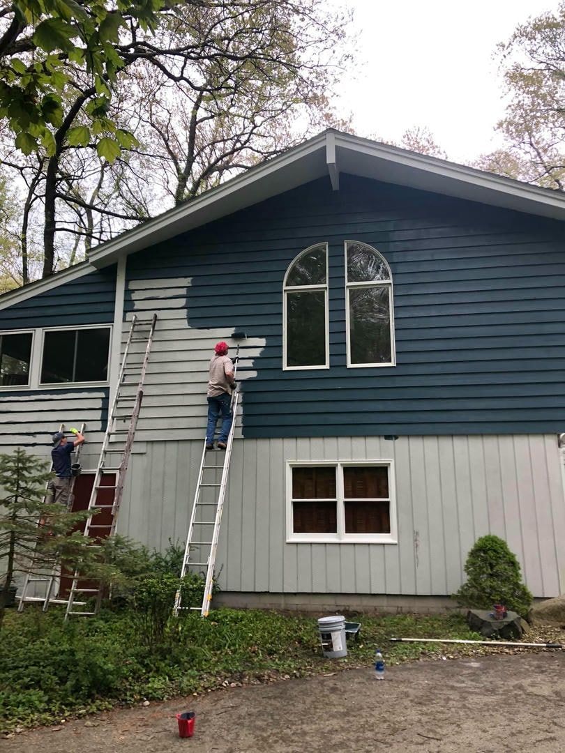 A man is standing on a ladder painting the side of a house.
