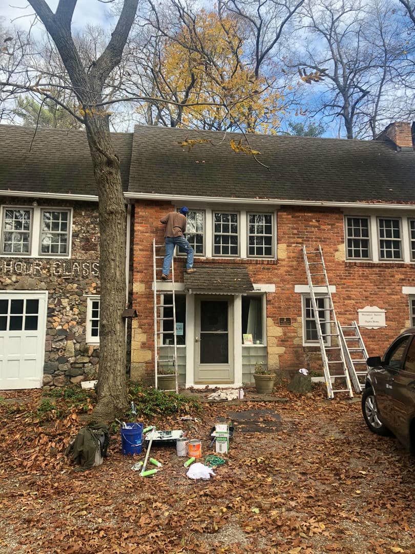 A man is painting the roof of a brick house.