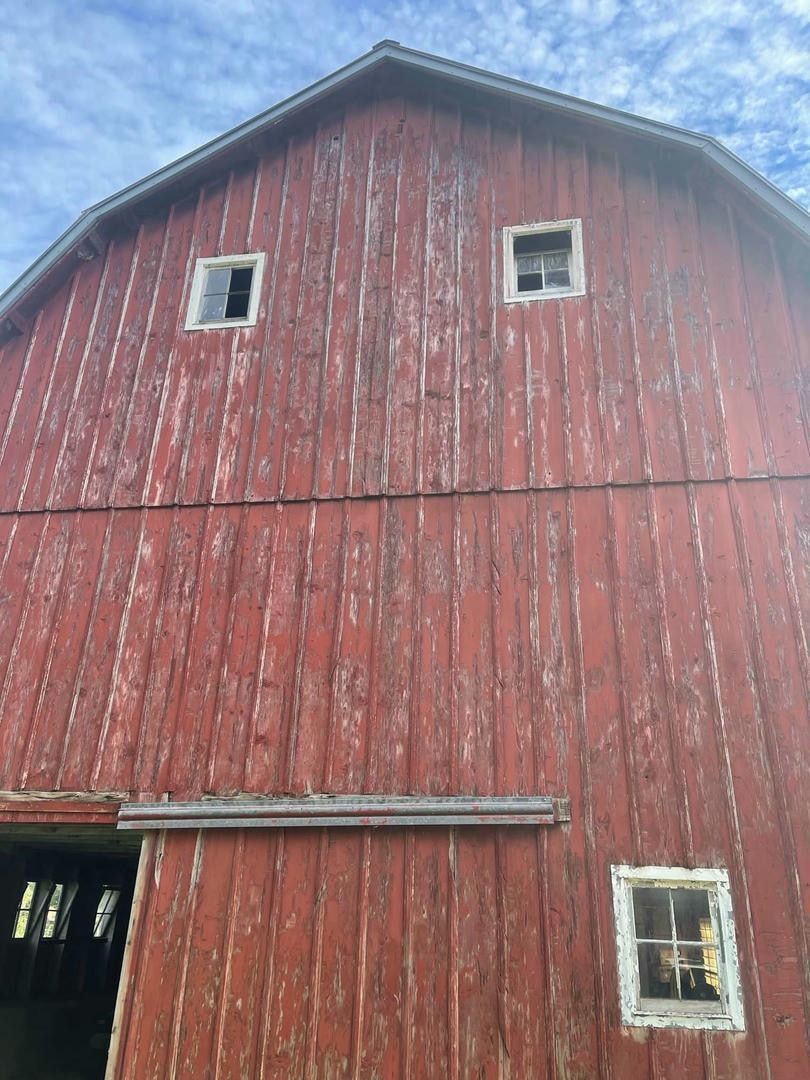 A red barn with two windows and a roof on a sunny day.