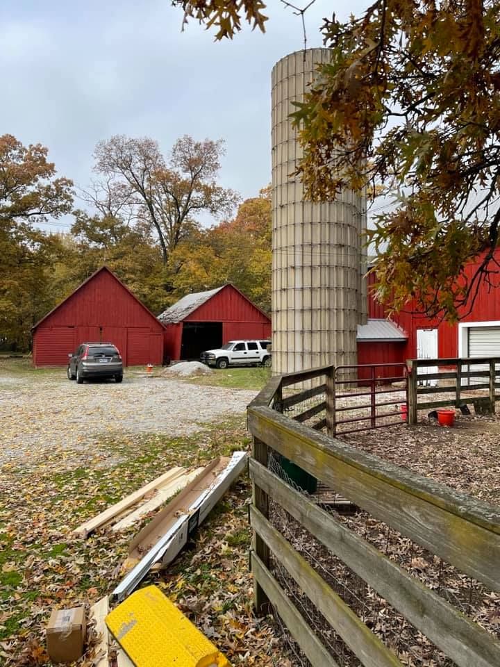 A fence surrounds a farm with red barns and silos.