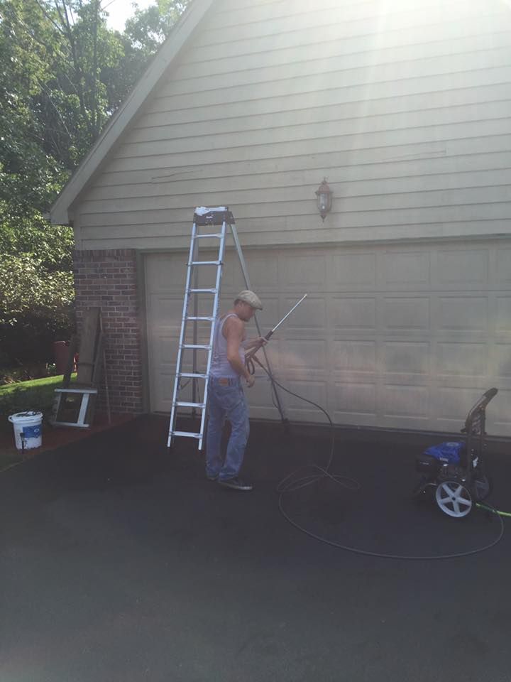 A man is standing on a ladder cleaning a garage door with a pressure washer.