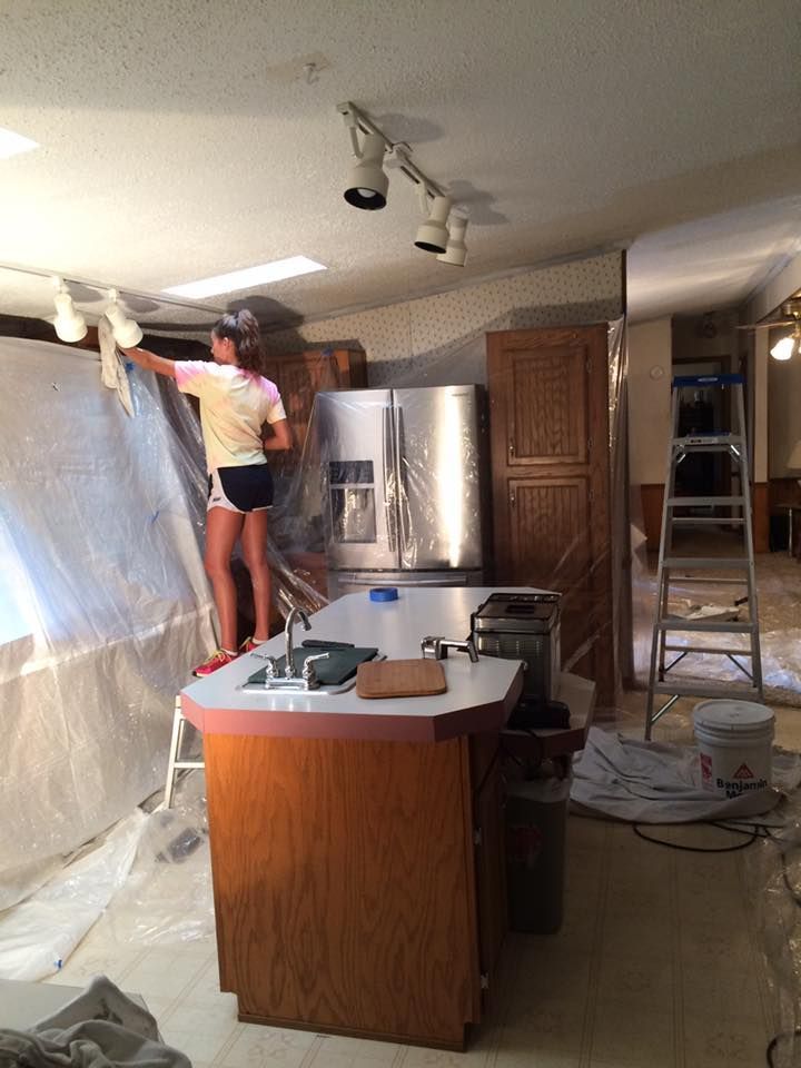A woman is standing on a ladder in a kitchen painting the ceiling
