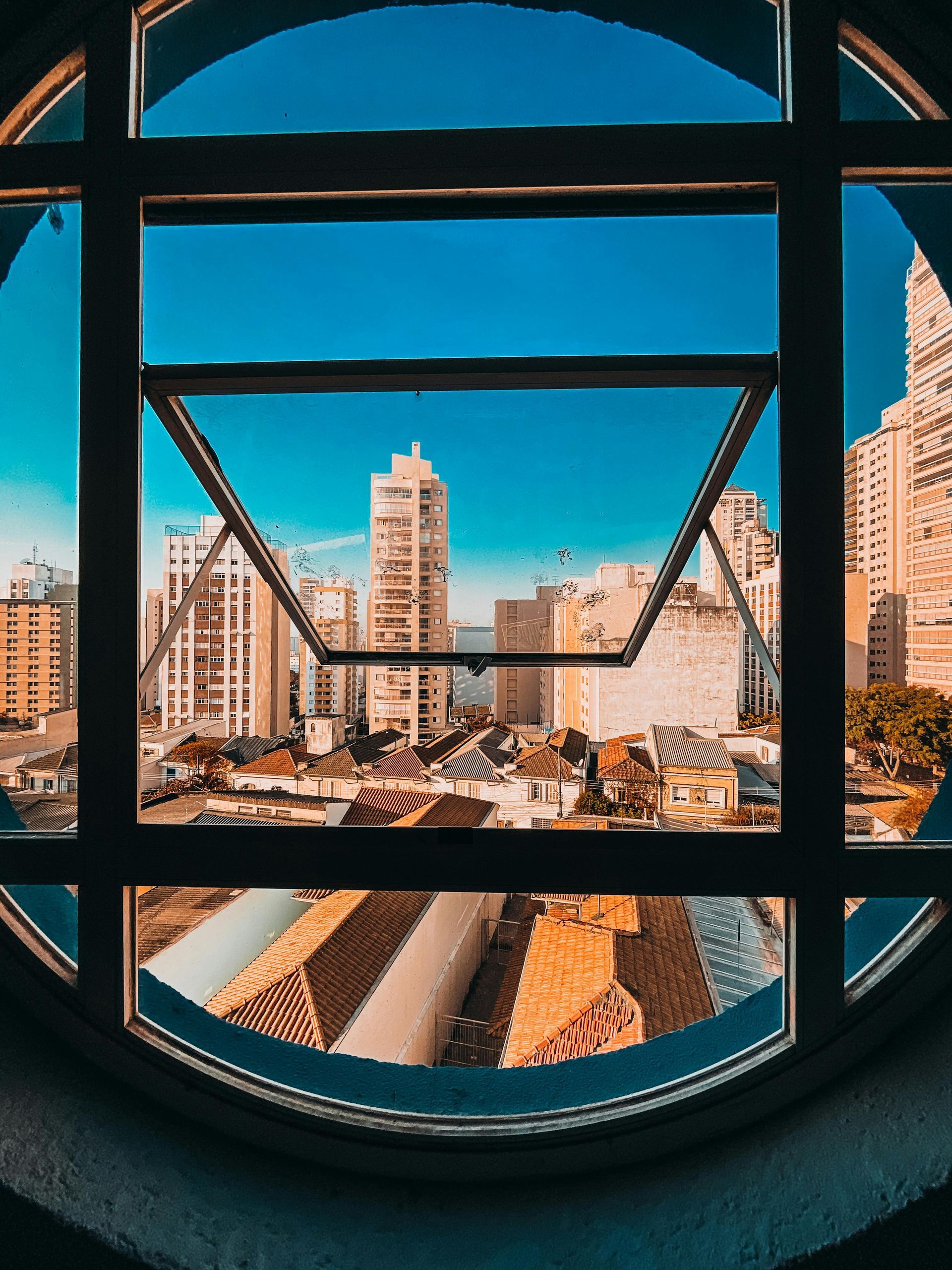 City skyline seen through a round window, with blue sky and tan buildings above railroad tracks.