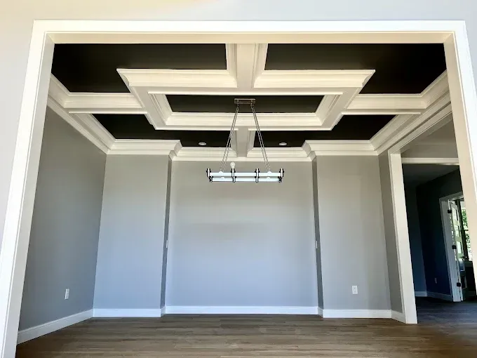 Dining room with a gray wall, white trim, black ceiling, and chandelier.
