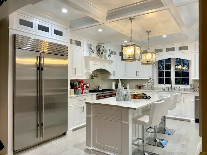 White kitchen with stainless steel fridge, island with bar stools, and pendant lights.
