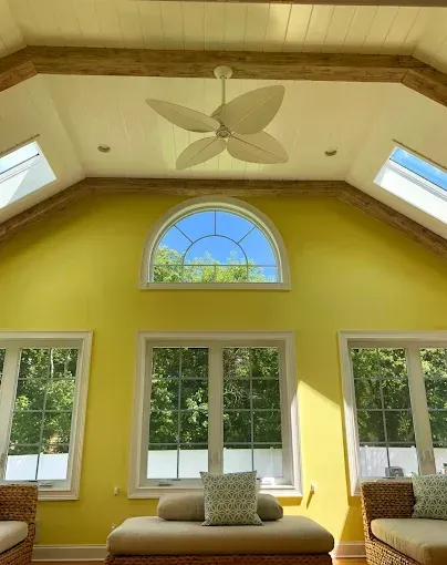 Bright yellow sunroom with windows, a fan, and a blue sky visible.