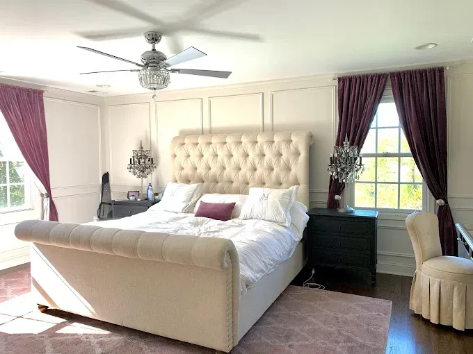 Bedroom with tufted bed, purple drapes, ornate lighting, and a matching chair.