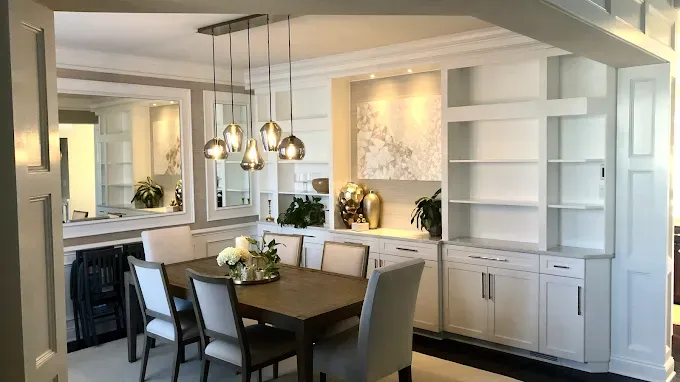 Dining room with table, chairs, built-in shelves, and hanging lights. White and light-colored decor.