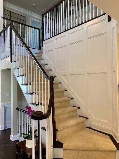 Staircase with white spindles, dark wood handrails, beige carpet, and white paneled walls.