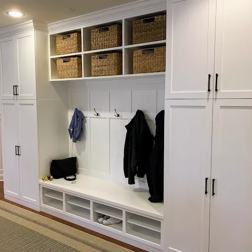 White built-in mudroom with bench, hooks, and storage baskets. Coats and bags hang.