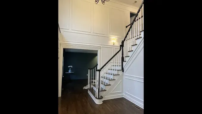 Entryway with staircase: white walls, dark handrail, stairs, doorway to a room with dark walls.