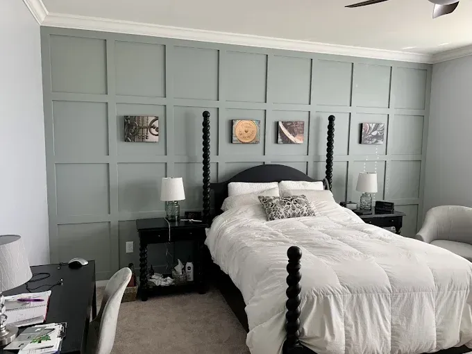 Bedroom with gray paneling, black bed, and artwork.