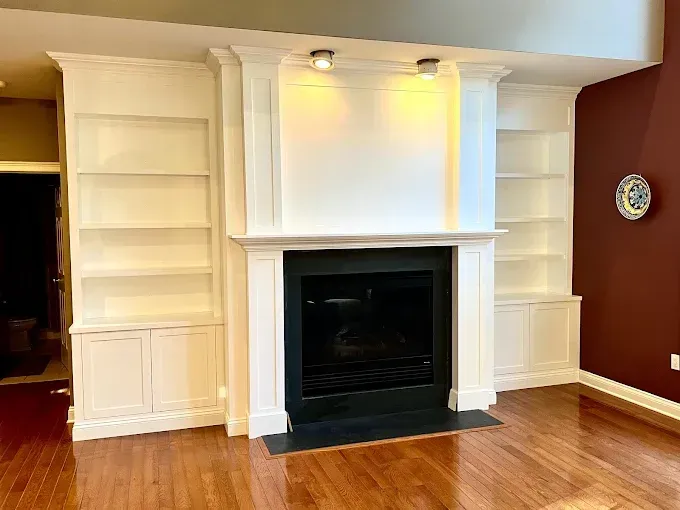 Built-in white bookshelves and fireplace on wood floor against maroon wall, with black fireplace interior.