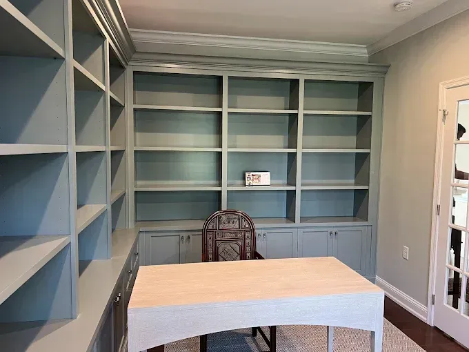 Built-in blue bookshelves surrounding a desk, with a chair and doorway, in a home office.