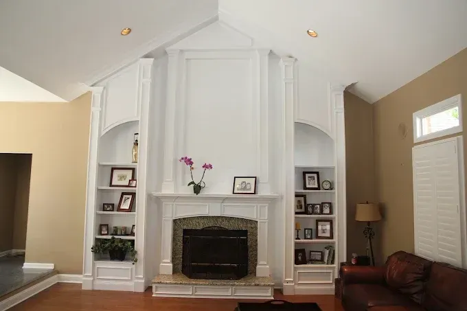 White fireplace with built-in bookshelves on either side. Tan and brown walls. Wooden floor.