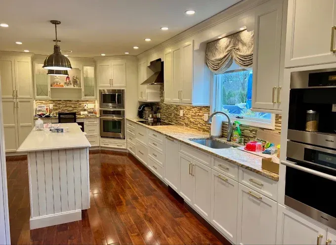 Bright, modern kitchen with white cabinets, wood floor, island, and granite countertops.