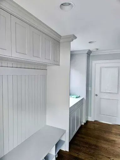 White built-in mudroom storage with bench, cabinets, and door in a hallway with wood flooring.