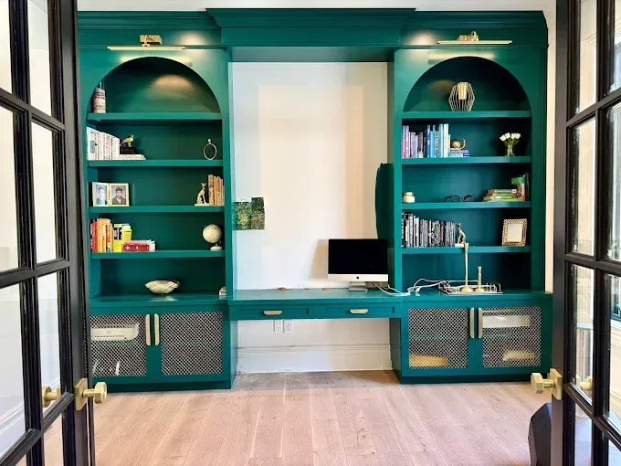 Green built-in home office with bookshelves, desk, and metallic door accents.