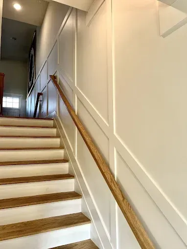 Staircase with wooden steps and handrail, white paneled walls.