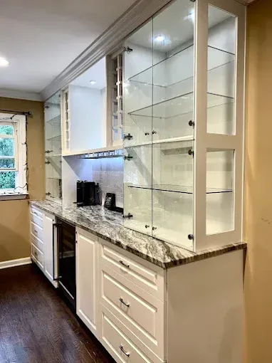 White built-in bar with glass-front cabinets, granite countertop, and a wine fridge.