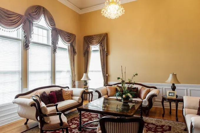 Elegant living room with cream sofas, gold walls, ornate curtains, and crystal chandelier.