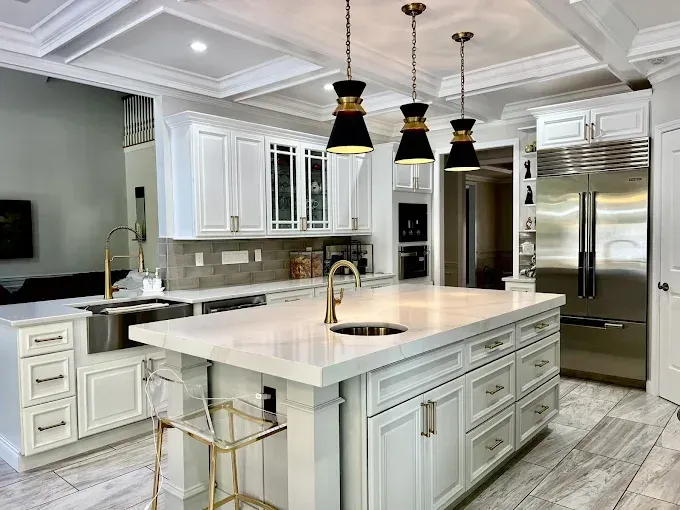 Elegant white kitchen with island, gold accents, pendant lights, and stainless steel appliances.