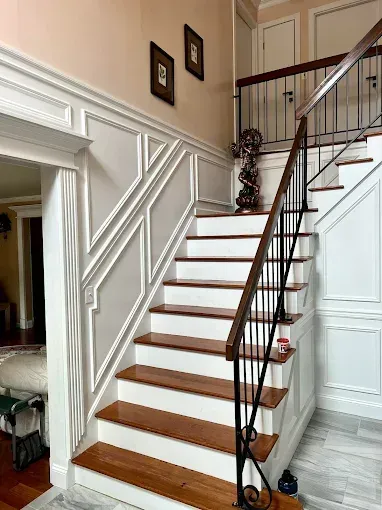 Staircase with white paneling and brown wooden steps, black railing, and decorative accents.