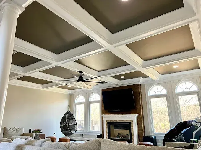 Living room with coffered ceiling, dark panels, white trim, fireplace, TV, large windows.