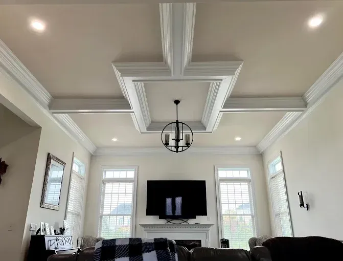 Living room with ornate ceiling beams, chandelier, fireplace, and large TV.