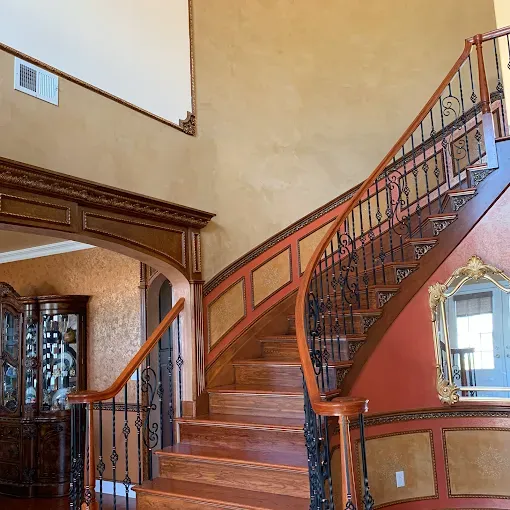 Wooden staircase with ornate iron railings. Decorative wall panels and gold accents.