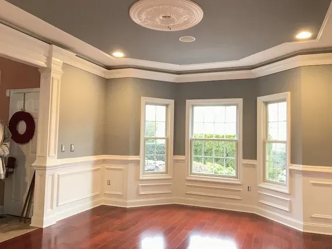 Dining room with gray walls, white trim, wood floors, and three windows.