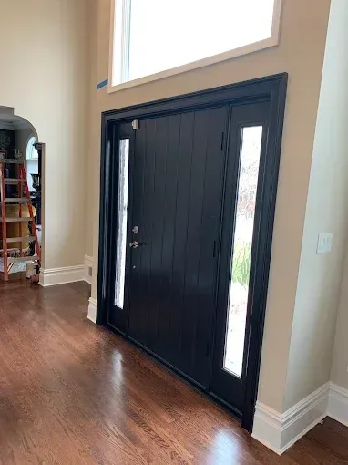 Black front door with sidelight, light-colored walls, hardwood floor.