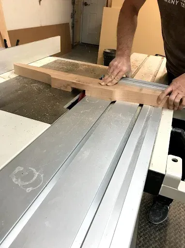 Person using a table saw to cut a piece of wood in a workshop.