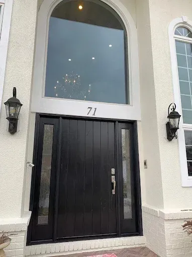 Black front door with sidelights and large arched window above, house number 71.