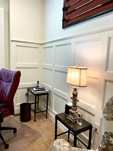 Office corner with paneled walls, a burgundy chair, lamps, and small tables.