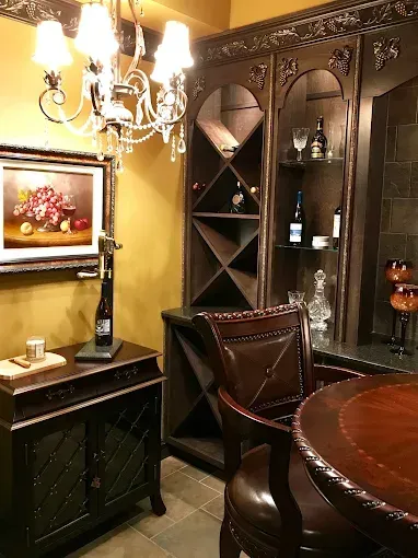 Dark wood wine cabinet and bar with chandelier, leather chair, artwork, and round table.