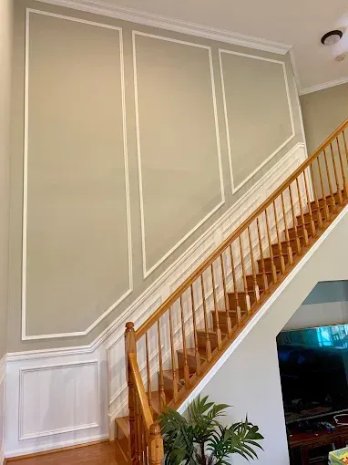 A two-story staircase with wood banisters and trim work on a neutral-colored wall.