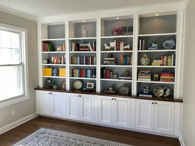 Built-in white bookshelves filled with books and decor above lower white cabinets, set in a room.