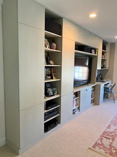Built-in entertainment unit with cabinets, shelves, desk, and TV. Pale green paint, beige carpet, and a pink rug.
