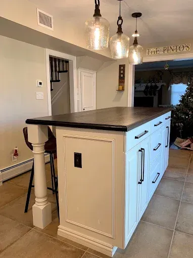 Kitchen island with white cabinets, dark countertop, three pendant lights, and a decorative support column.