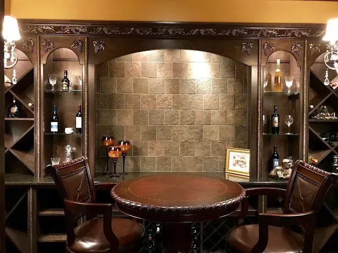 Wine bar with dark wood cabinetry, round table, leather chairs, and tiled backsplash.