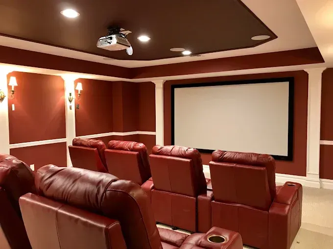 A home theater with red leather recliners, large screen, and maroon walls.