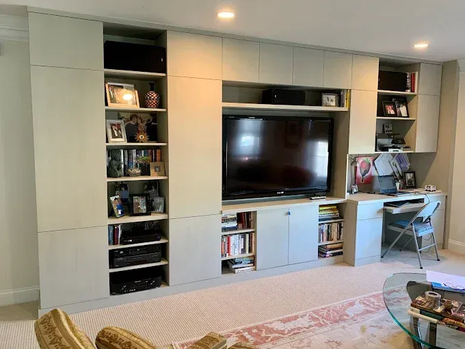 Built-in cabinet unit with a TV, shelves with items, and a desk in a living room.