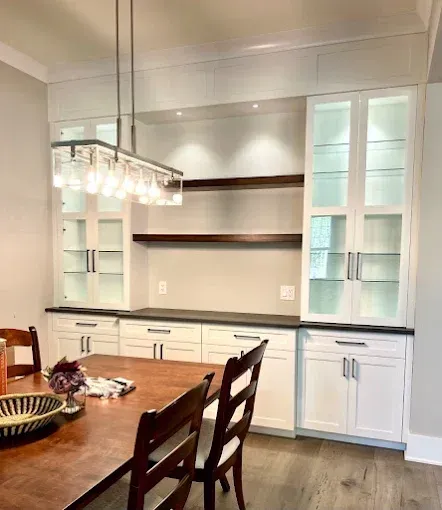 Dining room with white cabinets, dark shelves, a chandelier, and a wooden table.