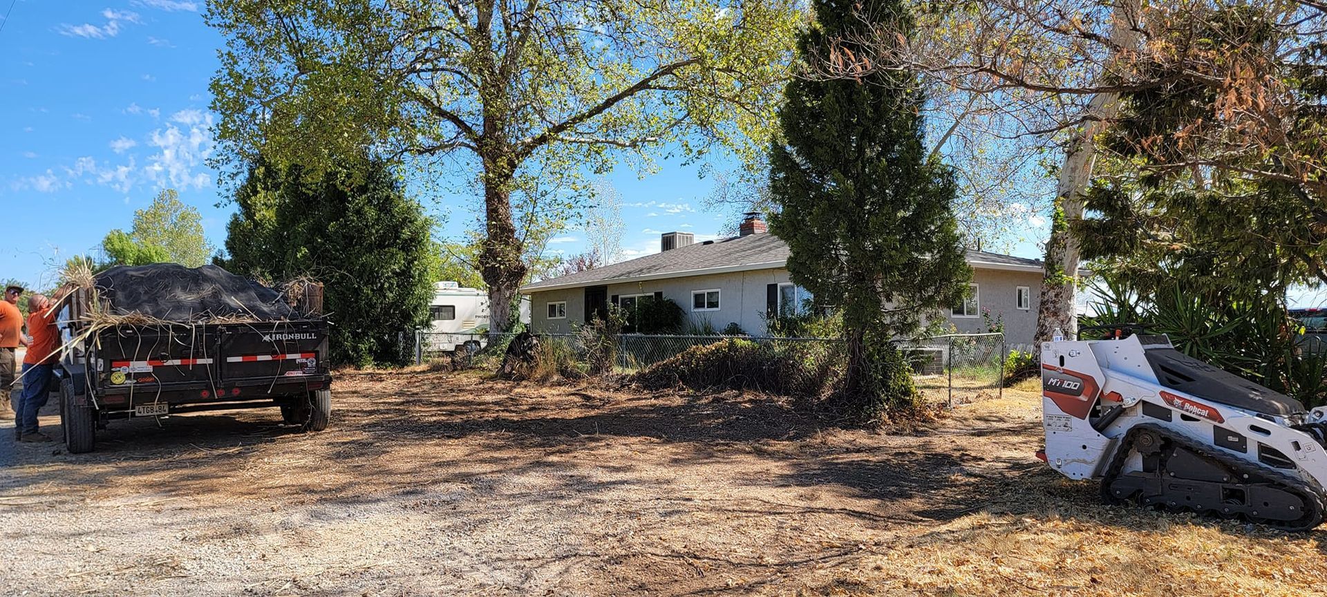 A trailer and a small excavator in front of a house, clearing debris.