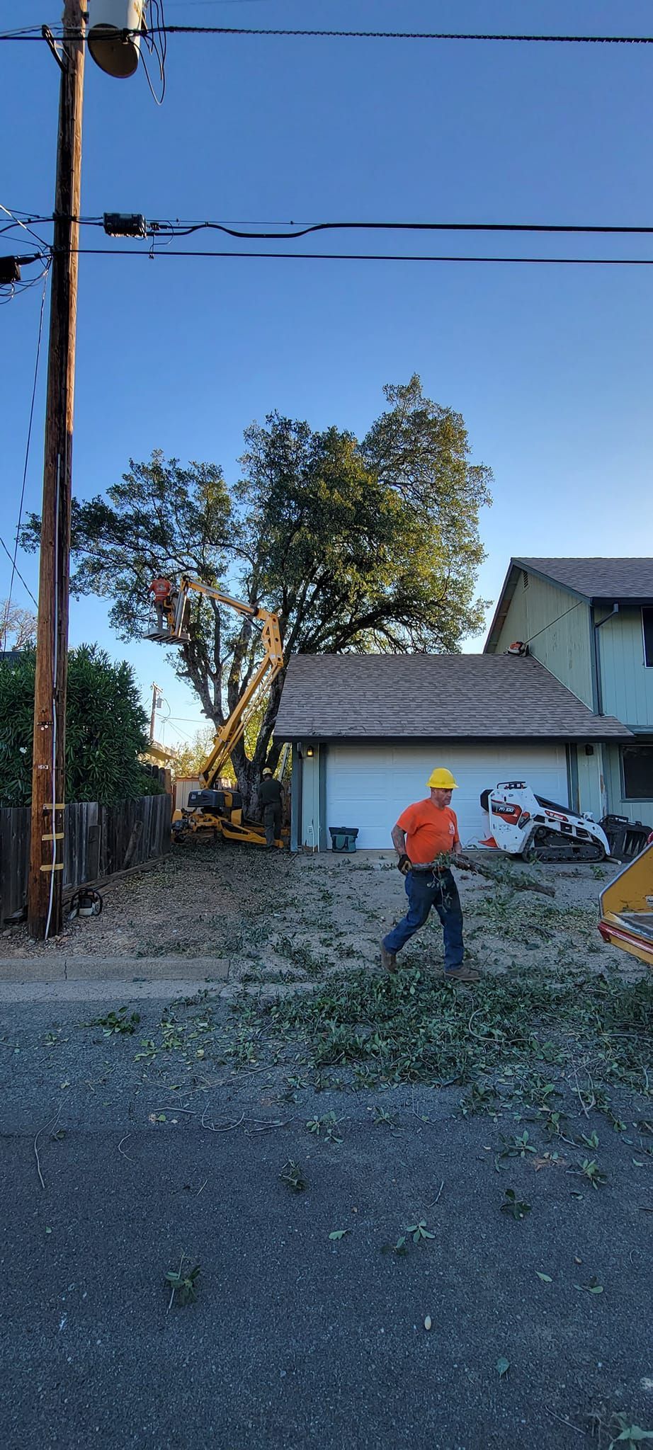 A person in an orange shirt and hard hat walks amidst leaves near a garage.
